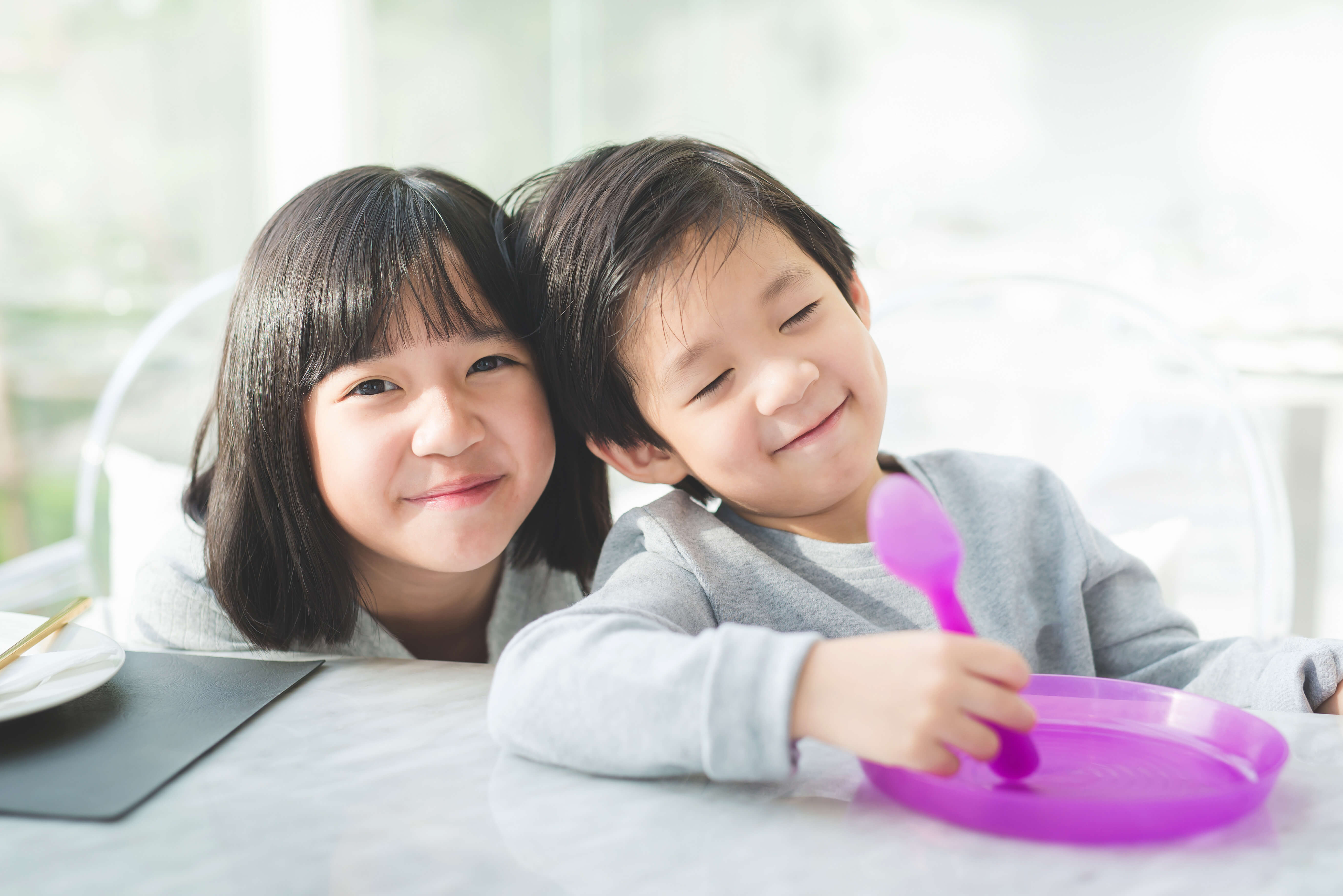 テーブルで一緒に遊ぶ二人の子供。紫色の食器を使って楽しそうな様子