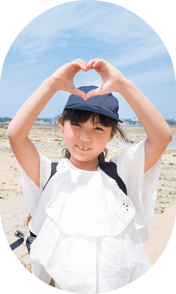 砂浜で手でハートを作る紺色の帽子をかぶった子供
