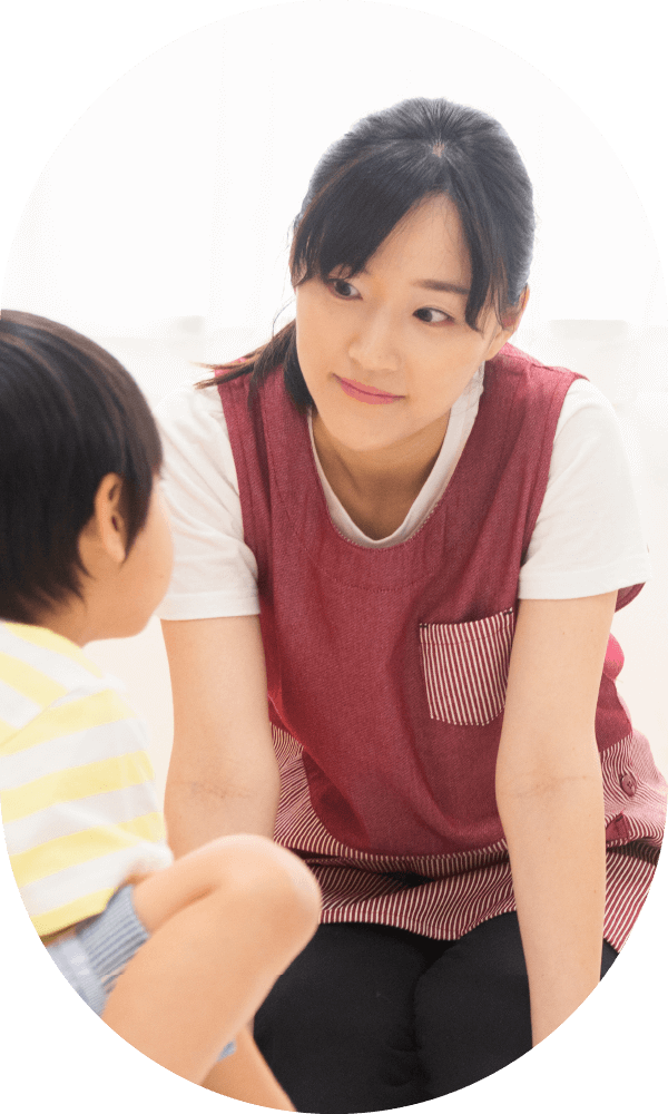 赤いエプロン姿で子供に優しく接する保育士